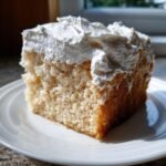 Close-up of a moist slice of Irresistible Homemade Tres Leches Cake topped with fluffy white whipped cream.