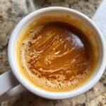 Close-up of rich, orange Irresistible Caramel Apple Cider swirling with cream in a white mug.