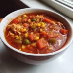 Close-up of a rich, tomato-based Brunswick Stew recipe filled with shredded chicken, corn, carrots, and peas.