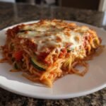 A close-up serving of Irresistible Veggie Packed Spaghetti Bake, topped with bubbly, melted mozzarella cheese and visible zucchini slices.