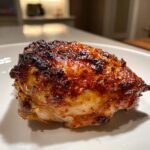 Close-up of a juicy, caramelized Irresistible Yogurt Marinated Chicken Thigh on a white plate.