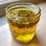 Close-up of Zesty Greek Salad Dressing Recipe ingredients mixed in a small glass jar.