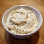 Close-up of a small white bowl filled with thick, creamy Zesty Horseradish Sauce on a wooden surface.