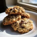 A stack of golden brown 4 Ingredient Chocolate Oat Cookies with visible oats and melted chocolate chips on a white plate.