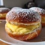 A close-up of an amazing Bomboloni Alla Crema filled with rich pastry cream and dusted heavily with powdered sugar.