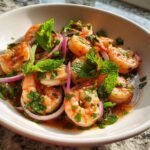 Close-up of Authentic Spicy Thai Shrimp Salad featuring plump shrimp, red onion slices, and fresh mint leaves in a savory dressing.