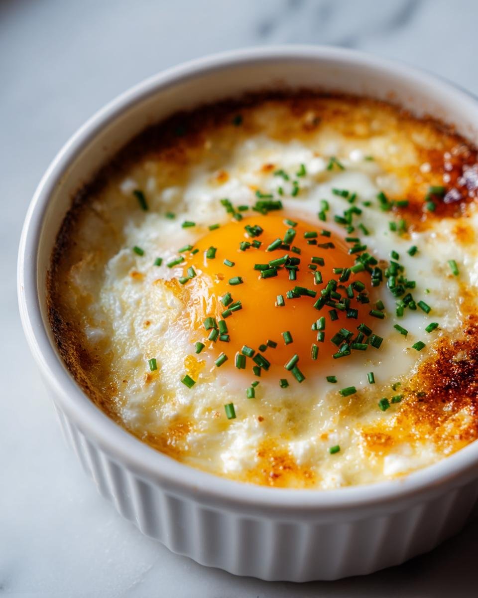Close-up of a single serving of Baked Cottage Cheese Eggs topped with a bright orange yolk and fresh chives.