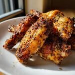 Close-up of crispy, golden Baked Lemon Pepper Chicken Wings heavily seasoned with cracked black pepper.