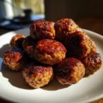 A close-up shot of a pile of beautifully browned and glazed Bison Meatballs resting on a white plate.