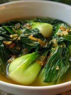 A close-up of vibrant green Bok Choy Soup With Garlic And Ginger served in a white bowl with savory broth.