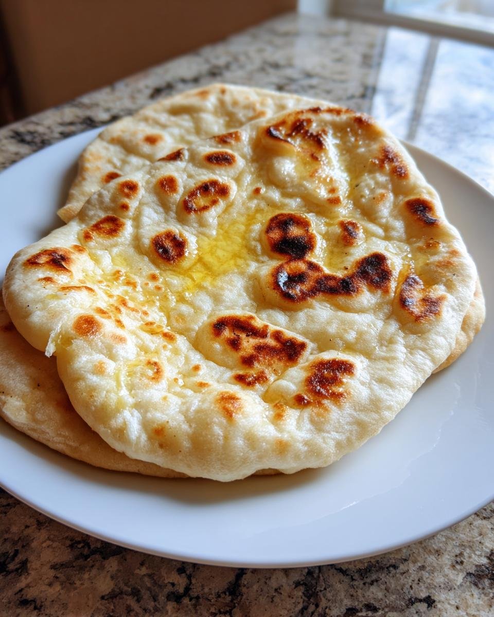 Two pieces of freshly cooked Gluten Free Naan Bread, brushed with melted butter, resting on a white plate.
