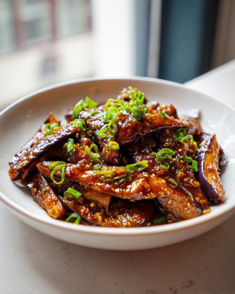 Close-up of glossy Chinese Eggplant With Garlic Sauce, topped with fresh green scallions.