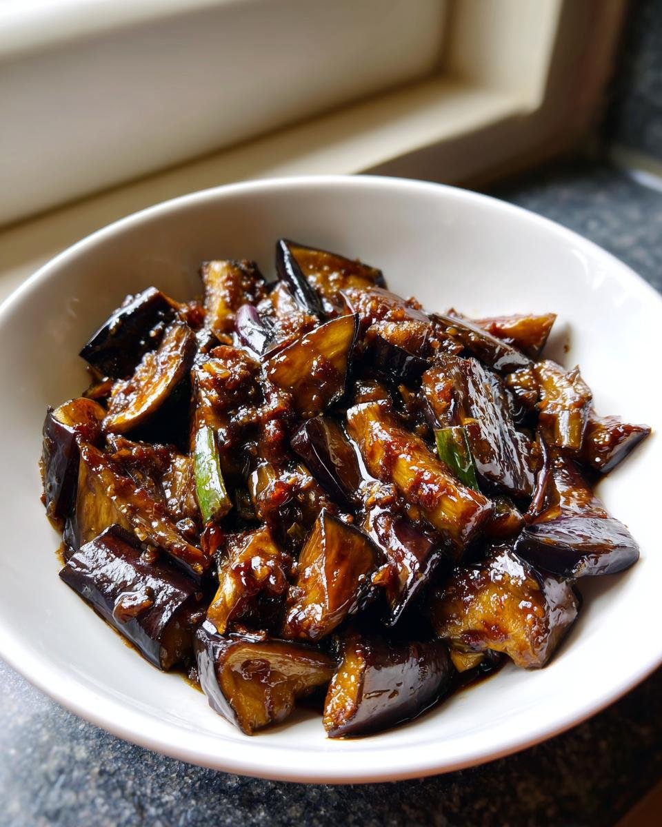 Close-up of glossy, saucy Chinese Eggplant With Garlic Sauce pieces served in a white bowl.