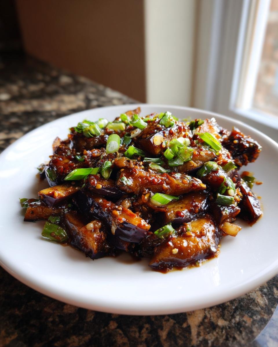 A plate of glossy Chinese Eggplant With Garlic Sauce topped with fresh green onions.