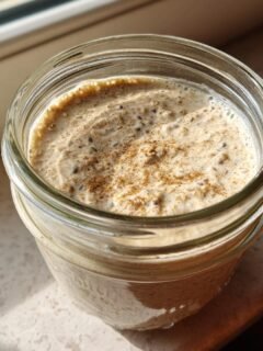 Overhead view of creamy Coconut Milk Overnight Oats topped with cinnamon in a glass jar, sitting in sunlight.