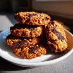 A stack of five freshly baked Crispy Chocolate Oat Cookies with melted chocolate chunks, sitting on a small white plate.