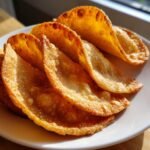 Close-up of several golden, crispy oven baked tacos shells arranged on a white plate.