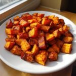 A white plate piled high with perfectly browned and Crispy Roasted Sweet Potatoes cubes catching the sunlight.