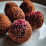 Close-up of Decadent Dark Chocolate Raspberry Truffles dusted in cocoa powder, some topped with freeze-dried raspberry pieces.