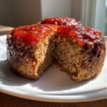 A single Easy Mini Meatloaf Whole30, cut open to show the texture, topped with a bright red glaze.