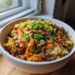 A white bowl filled with Egg Roll In A Bowl, featuring ground meat, cabbage, carrots, and green onion garnish.