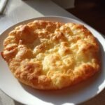 A close-up of freshly cooked, golden brown fry bread with puffy, uneven surfaces resting on a white plate.