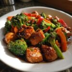 Close-up of glossy, glazed chunks of salmon mixed with bright green broccoli and red peppers in a Salmon Stir Fry.