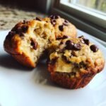 A Gluten Free Banana Chocolate Chip Muffin broken in half showing moist interior and chocolate chips.