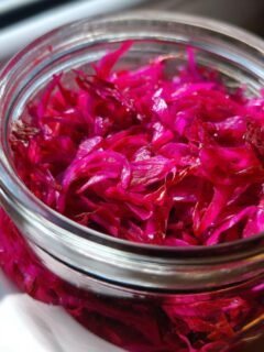 Close-up of bright pink/purple pickled onions filling a glass jar, ready for Gordon Ramsay Pickled Onions Recipe.
