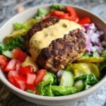 A close-up of a Healthy Burger Bowl With Special Sauce featuring a seasoned patty topped with sauce over fresh lettuce, tomatoes, pickles, and onions.