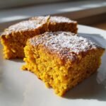 Close-up of moist, orange-colored Healthy Pumpkin Bars dusted lightly with powdered sugar on a white plate.