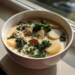 Close-up of a white bowl filled with creamy Healthy Zuppa Toscana featuring sausage, sliced potatoes, and bright green kale.