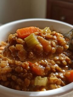 A spoonful of thick, rich Hearty Crockpot Lentil Soup featuring visible carrots and celery being lifted from a white bowl.
