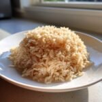 A mound of perfectly cooked Instant Pot Brown Jasmine Rice served on a white plate, highlighted by natural sunlight.