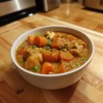A close-up of a white bowl filled with rich Instant Pot Chicken Stew featuring chunks of chicken, carrots, and peas.