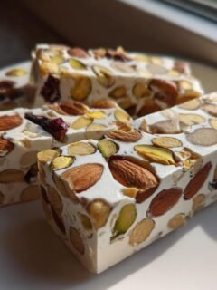 Close-up of thick slices of The Best Italian Torrone, packed with whole almonds and pistachios, sitting on a white plate.