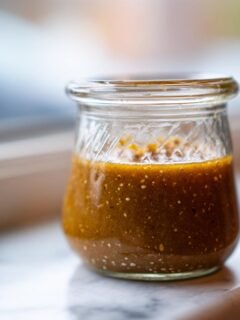 A small glass jar filled with rich, textured Japanese Ginger Salad Dressing sitting on a white marble surface.