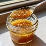 A spoonful of thick, textured Japanese Ginger Salad Dressing being lifted from a small glass jar.