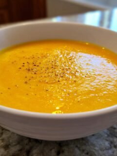 Close-up of bright orange Mango Gazpacho garnished with cracked black pepper in a white bowl.
