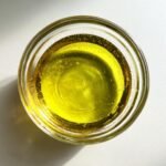 Overhead view of bright yellow oil in a small glass bowl, an ingredient for Honey Lime Dressing.