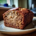 A close-up, appetizing shot of a thick slice of freshly baked Paleo Banana Bread sitting on a light green plate.
