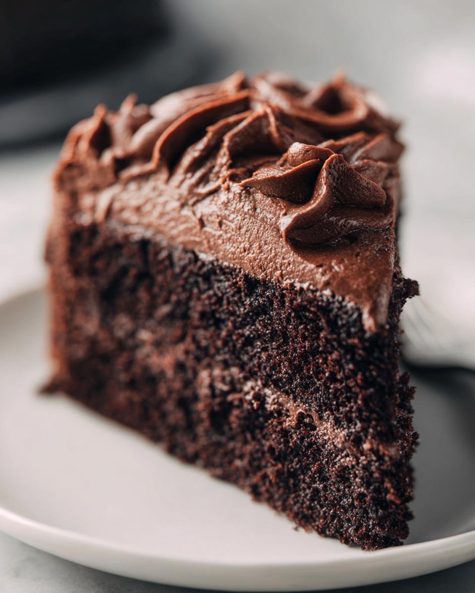 Close-up of a rich slice of Paleo Chocolate Cake With Whipped Chocolate Frosting on a white plate.