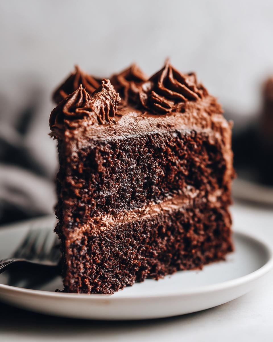Close-up of a rich, dark slice of Paleo Chocolate Cake With Whipped Chocolate Frosting on a white plate.