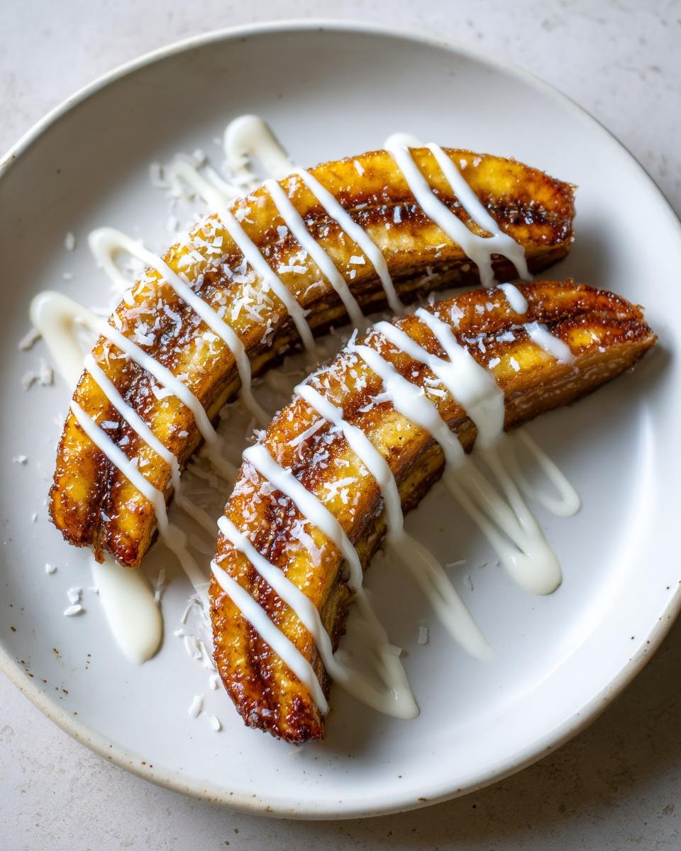 Two halves of Pan Fried Bananas With Coconut Cream drizzled with white sauce and sprinkled with coconut flakes.