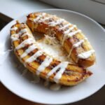 Two halves of Pan Fried Bananas With Coconut Cream drizzled on a white plate.