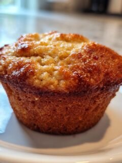 A single, perfectly golden-brown Protein Banana Muffin sitting on a white plate.