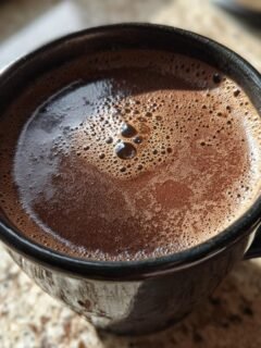 Close-up of a dark, foamy Protein Hot Chocolate Recipe served in a black mug.