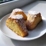 Three triangular slices of golden Sherlock Holmes Foggy London Tea Cakes dusted generously with white powdered sugar on a white plate.