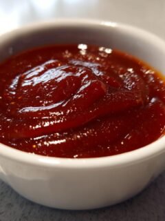 Close-up of thick, glossy, dark red Shut Yo Mouth Sauce served in a small white dipping bowl.