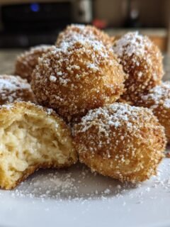 A plate of golden brown, fried Slovenian Farmers Cheese Dumplings dusted generously with powdered sugar.